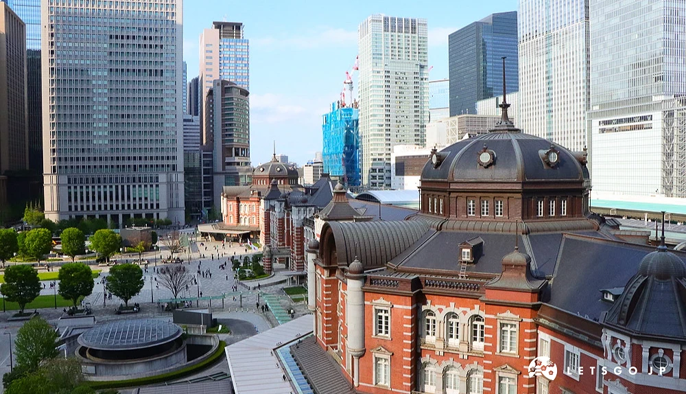 從高處俯瞰東京車站紅磚建築,背景為丸之內密集的摩天大樓群。